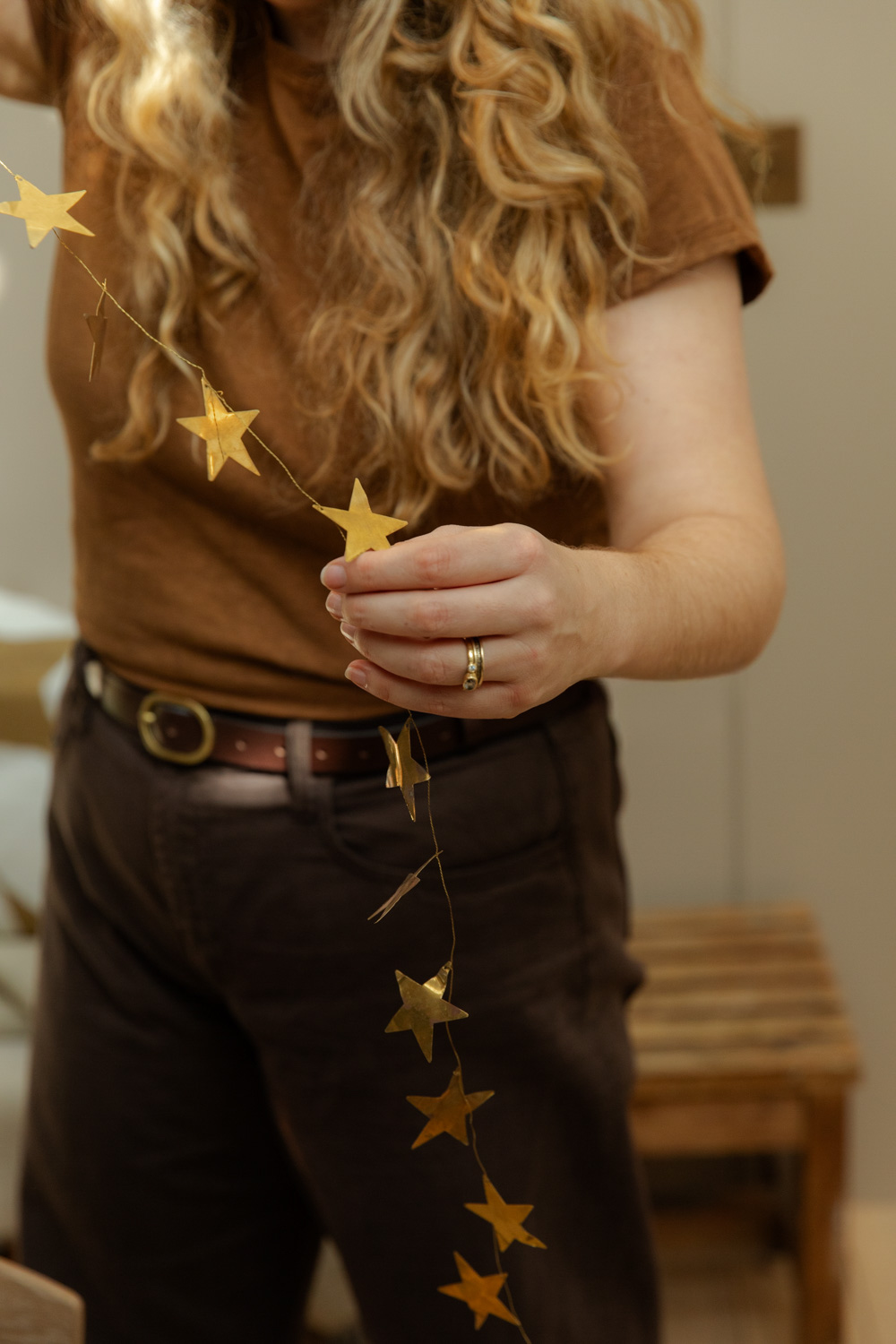 Alice is wearing tones of brown and is holding a brass star garland in front of her body